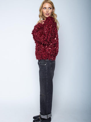 Junge Frau im Profil trägt Emily Blouson 201270-10 bordeaux mit Pailletten- und Federeffekt, kombiniert mit dunkelblauen Jeans und schwarzen Loafern, präsentiert die stilvolle Textur des Blousons.