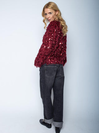 Eine Frau trägt den Emily Blouson 201270-10 bordeaux mit Zipper-Verschluss, glänzenden Pailletten und Federeffekt, kombiniert mit dunklen Jeans und schwarzen Loafers.