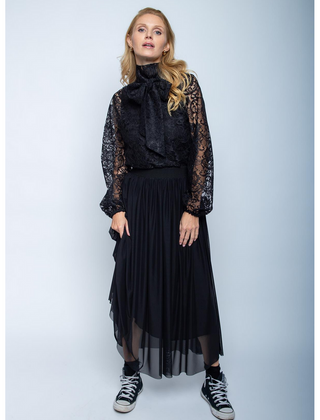 Frau trägt Emily Rock 201451 black: schwarzer, ausgestellter Mesh-Rock mit Gummibund, offener Saumkante, kombiniert mit schwarzer Spitzenbluse. Vervollständigt mit schwarzen High-Top-Sneakers.