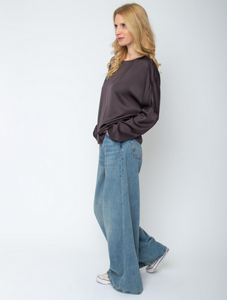 Emily Bluse 157490-10 chocolate aus fließendem Viskose-Satin mit rundem Ausschnitt und modernen, überschnittenen Schultern. Getragen von Frau in weiter, hellblauer Jeans, Hände in Hosentaschen.