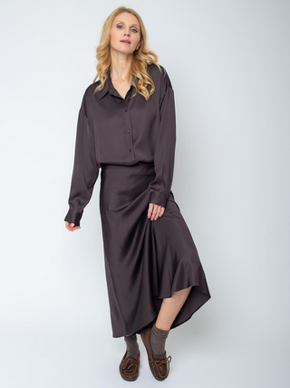 Frau trägt Emily Rock 201460-10 chocolate, ein moderner, leicht ausgestellter Rock aus fließender Viskose mit elastischem Bund, kombiniert mit passender Bluse. Ergänzt durch braune Mokassin-Slipper.