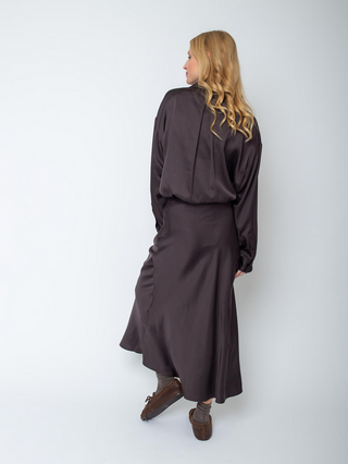 Emily Bluse 155923-10 chocolate aus fließendem Viskose-Satin, oversized mit überschnittener Schulter und Knopfblende. Gesehen von hinten, kombiniert mit passendem Rock und mokassinartigen Schuhen.