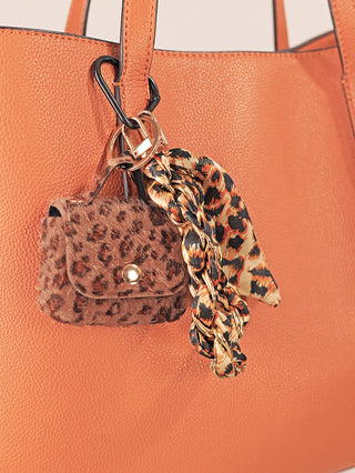 Nahaufnahme des OFF#DLY Taschenanhänger Leo brown, einem kleinen Leopardenmuster-Faux-Fur-Beutel mit goldener Kette und animal-print Schal, befestigt an einer orangefarbenen Lederhandtasche.