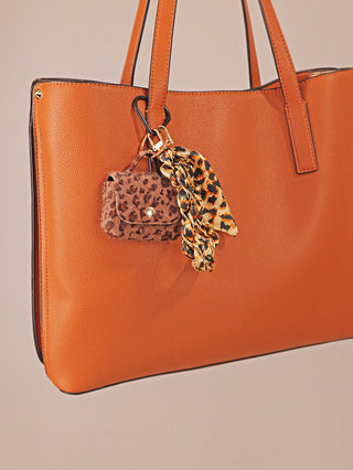 OFF#DLY Taschenanhänger Leo braun: Strukturierte Handtasche mit Leo-Anhänger, bestehend aus einem flauschigen Beutel, einer goldfarbenen Kette mit Band und einem Leoparden-Schal, alles harmonisch kombiniert.