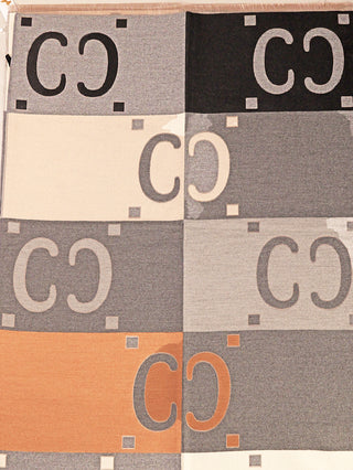 OFF#DLY Schal C.C. grau/beige zeigt große, rechteckige Paneele mit „C C“-Motiven und kleinen Quadrat-Akzenten, aufgehängt zur Präsentation. Hergestellt aus Viskose, Wolle und Kaschmiranteil.