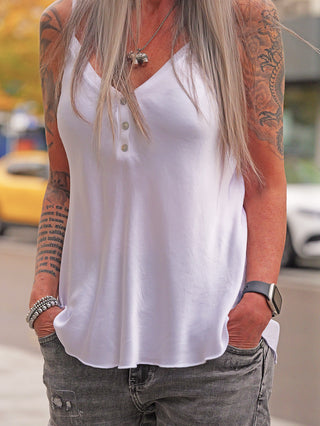 Person trägt das OFF#DLY Top Button white aus fließender Viskose mit Knopfleiste. Sichtbare Tattoos und Armbänder ergänzen den Look. Träger sind nicht verstellbar.