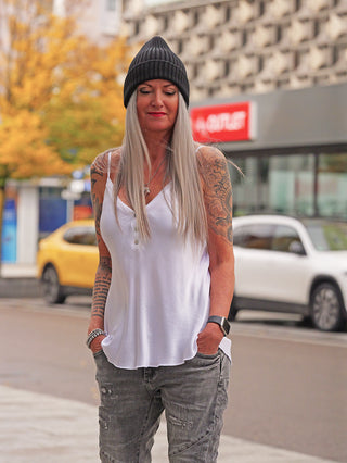 Erwachsener trägt ein OFF#DLY Top Button white, ein luftiges, trägerloses Viskose-Top mit Knopfleiste und elastischem Bund, kombiniert mit grauen Jeans auf einem Bürgersteig.