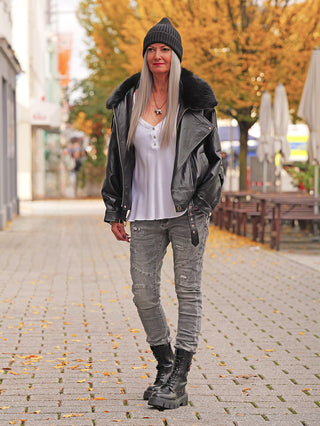 Frau trägt OFF#DLY Destroy Denim Rosella grey, eine körperbetonte graue Jeans mit leichten Destroy-Details. Kombiniert mit schwarzer Lederjacke und Plattformstiefeln, perfekter urbaner Streetstyle-Look für den Herbst.