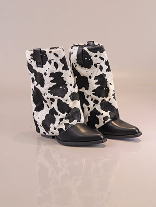 OFF#DLY Cow Boot black/white mit spitzen schwarzen Lederzehen und schwarz-weißem Kuhfellmuster, seitlicher Reißverschluss für einfachen Einstieg, mittelhoher Schaft und Absatz auf reflektierender Oberfläche.