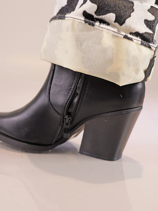 Der OFF#DLY Cow Boot black/white zeigt sich als schwarzer, glatter Stiefelette mit seitlichem Reißverschluss, kombiniert mit hochgerollten, schwarz-weiß gemusterten Hosenaufschlägen.