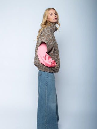 Emily Damenjacke 201481 leo: Die junge Frau trägt eine lockere, braune Fuzzy-Weste mit subtilen Leopardenmuster über einem langärmligen rosa Oberteil, kombiniert mit blauer Denim, Hände in den Westentaschen.