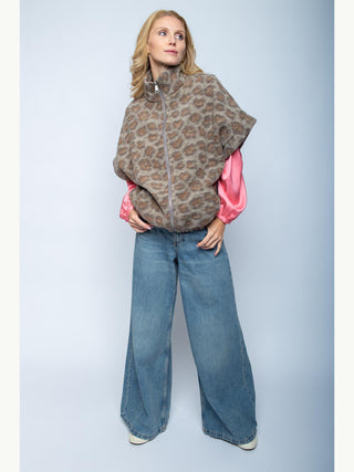 Emily Damenjacke 201481 leo: Frau trägt eine kurzärmelige, zip-front Poncho-Jacke mit Stehkragen im animalischen Muster, kombiniert mit weiten blauen Jeans. Darunter leuchten pinke Satinärmel hervor.