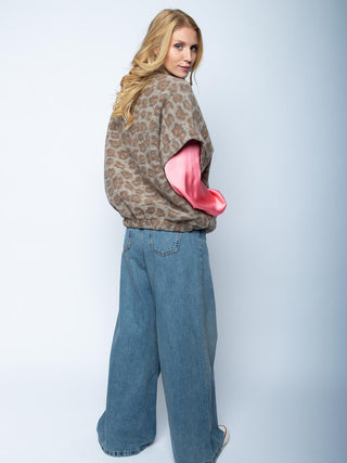 Emily Damenjacke 201481 leo: Eine junge Frau trägt eine lockere, flauschige, ärmellose Weste mit Leopardenmuster über einem pinken Langarmshirt, kombiniert mit hochgeschnittenen, weit geschnittenen blauen Jeans und weißen Sneakern.