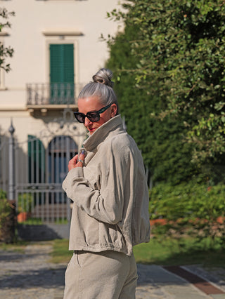 Frau trägt die OFF#DLY Jacke Vera sand aus weichem Cord, mit lockerer Passform und Kragen, vor einer Villa. Ideal für Layering und Übergangszeit.