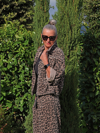Ältere Frau trägt die OFF#DLY Cordjacke Valerie taupe/leo mit coolem Leoparden-Print und lässigem Schnitt, ergänzt durch große schwarze Sonnenbrille und elegante Ohrringe, vor grüner Kulisse.