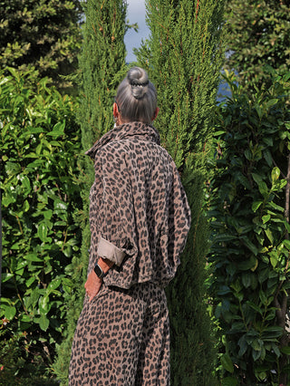 Person mit silbergrauem Dutt trägt OFF#DLY Cordjacke Valerie taupe/leopard in einem Garten. Die Jacke hat einen lässigen Leoparden-Print, weite Passform und elastischen Bund, sichtbar mit Smartwatch.