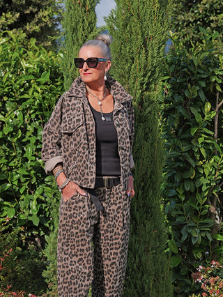 Frau trägt die OFF#DLY Cordjacke Valerie taupe/leo mit Leopardenprint, kombiniert mit passender Hose und schwarzem Tanktop, in einem Garten. Jacke hat Knopfleiste und elastischen Bund.