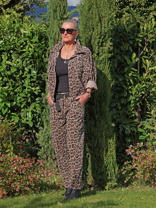 Frau trägt die OFF#DLY Cordjacke Valerie taupe/leo im lässigen Leoparden-Print, kombiniert mit passender Hose, schwarzen Accessoires und Boots, im Garten stehend.