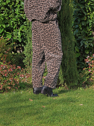 Person trägt OFF#DLY Pant Viola leo/taupe, eine locker geschnittene Cord-Hose mit Leo-Muster und elastischem Bund, stehend auf einem Rasen, kombiniert mit schwarzen Stiefeletten.