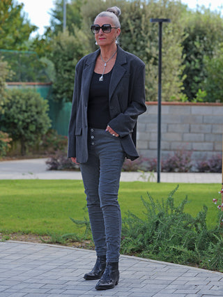 Frau im Freien in OFF#DLY Color Jeans Imelda grau, schlanke Passform mit Knopfdetails, kombiniert mit Blazer und Stiefeletten. Perfekt für stilvolle Alltags- oder elegante Casual-Outfits.