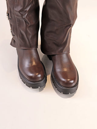 Nahaufnahme von OFF-DLY Biker Boot dark Brown; dunkle braune Lederstiefel mit seitlichem Reißverschluss, klobiger, profilierter schwarzer Sohle, kombiniert mit braunen Leggings oder Chaps, auf hellem Hintergrund.