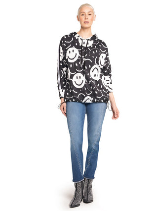 Frau in lockerem Doris Streich Shirt 349146 schwarz/weiß: Schwarzer Hoodie mit weißen Smiley-Motiven, Streifen an Ärmeln, kombiniert mit blauen Jeans und schwarzen Stiefeletten mit weißen Punkten.