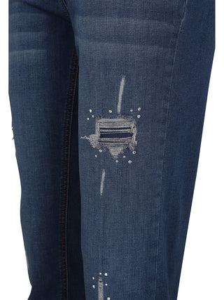 Nahaufnahme von Doris Streich Hose Denimblau: Dunkelblaue Jeans mit einem zerrissenen Patch am Oberschenkel, umgeben von kleinen Metallnieten oder Strasssteinen als dekorative Akzente, im Slim-Fit-Stil.