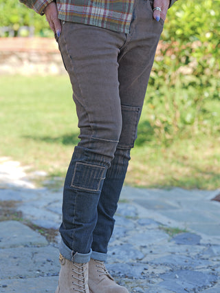 Person trägt OFF#DLY Sina Brown Wash Denim mit markanten Knie- und Wadenpatches, hochgekrempelten Bündchen und einem eingesteckten karierten Flanellhemd, kombiniert mit hellbraunen Schnürstiefeln auf einem Außenweg.