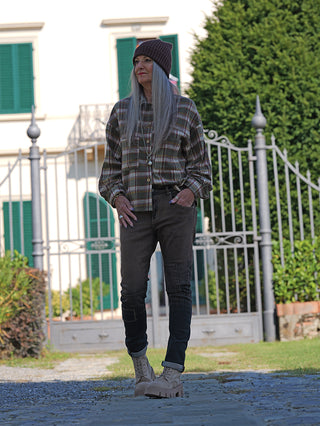 Frau trägt OFF#DLY Sina Brown Wash Denim mit modernem Schnitt und Used-Effekt. Kombiniert mit kariertem Hemd, beanie, klobigen Stiefeln, zeigt sie einen lässigen, stilvollen Look vor einem Haus.