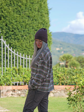 Person trägt die OFF#DLY Bluse Amelia multicolor, eine locker geschnittene, karierte Bluse mit Knopfleiste und Brusttaschen, ideal kombiniert mit dunkler Hose in einem natürlichen, parkähnlichen Umfeld.