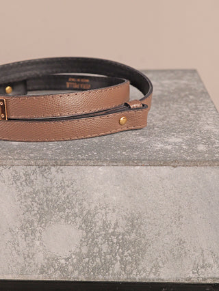 Der OFF#DLY Gürtel Leder taupe zeigt einen strukturierten, gewickelten Lederstreifen mit goldfarbener Schließe, liegend auf einem rauen Steinblock.