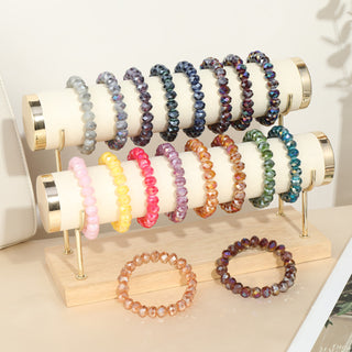 Ein kleines Display zeigt das Flaches Kristallperlen Armband dark pink 222 auf einem cremefarbenen, gepolsterten Ständer, umgeben von weiteren Armbändern in verschiedenen Farben.