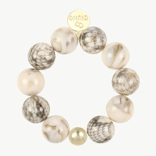 Kugelarmband Acryl Muschelfarben mit elastischen, marmorierten, cremeweißen und grauen Acrylperlen, ergänzt durch eine kleinere goldfarbene Perle und einem goldfarbenen Anhänger mit Logo.