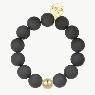 Acryl Kugelarmband black, ein dehnbares Armband mit mattschwarzen Kugeln, einem goldfarbenen Akzent und einem goldenen Anhänger mit GIUNO-Prägung. Kugeldurchmesser 15 mm, Material Acryl und Kupfer.