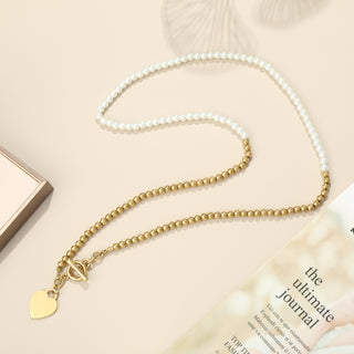 Edelstahl Perlenkette Herz white/gold auf beigem Untergrund; eine Hälfte aus weißen Perlen, die andere aus goldenen Perlen, mit Herzanhänger und Knebelverschluss, neben Geschenkbox und Zeitschrift.