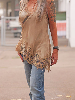 Person trägt OFF#DLY Top Violetta camel, ein locker fallendes, ärmelloses Spitzentop mit feiner Spitze am Ausschnitt. Kombiniert mit blauen Jeans, Schmuck und einer Smartwatch.