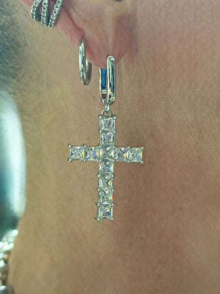 Nahaufnahme eines Ohres mit mehreren silbernen Creolen, darunter der OFF#DLY Ohrschmuck Kreuz silber mit einem anhängenden Kreuz, besetzt mit klaren, facettierten Steinen.