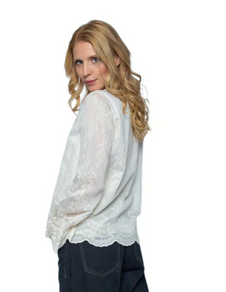 Emily Bluse 157110-10 offwhite/lace: Frau trägt eine langärmelige Bluse mit floralem Spitzenmuster und Bogenkante, kombiniert mit dunklen Jeans, perfekt für einen eleganten Look.