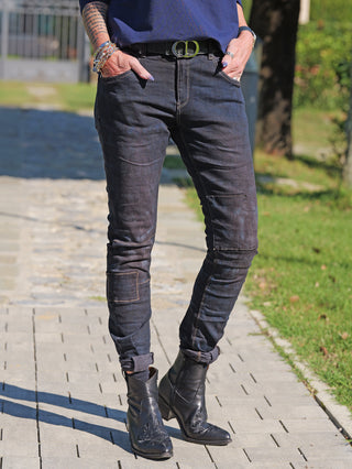 Person trägt OFF#DLY Denim Karin Dirty Wash Jeans mit schmalem Schnitt und Kniepatches, kombiniert mit schwarzen, bestickten Lederstiefeletten. Hände in Taschen, Gürtel sichtbar. Prachtvoller, urbaner Stil.