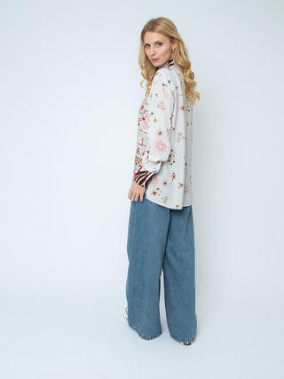 Emily Bluse 157202 sand/red/zebra: Frau trägt langärmlige Hemdbluse mit Stern- und Sonnenmotiven, kombiniert mit weiten Jeans. Lockeres Design, durchgehende Knopfleiste, fließende Viskose, kleine Creolen als Accessoire.