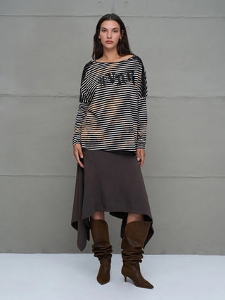 #VDR T-Shirt 18004 black/white: Locker sitzendes gestreiftes Longsleeve mit Bleach-Effekt, überschnittener Schulter und glitzerndem Logo. Kombiniert mit asymmetrischem Rock und kniehohen Stiefeln vor grauer Wand.