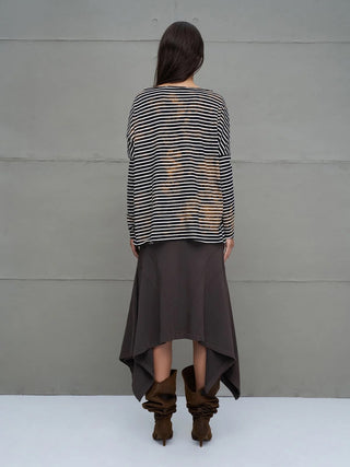 Person von hinten in #VDR T-Shirt 18004 black/white mit schwarz-weißen Streifen und Bleach-Effekt, kombiniert mit asymmetrischem Rock und braunen Stiefeln vor grauem Hintergrund.