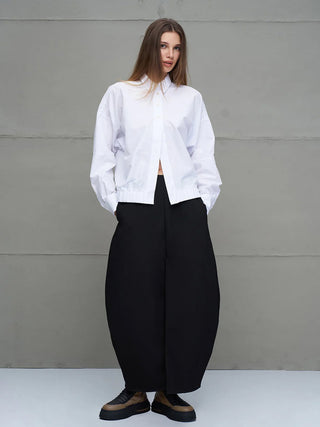 Junge Frau in #VDR Shirt 18231 white: eine weiße, oversized Bluse mit klassischem Hemdkragen, lockerem Schnitt und Schriftzug „Not Perfect But Myself“ auf dem Rücken, kombiniert mit weiten, schwarzen Rock-Hosen.