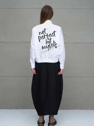Person von hinten trägt #VDR Shirt 18231 white mit Slogan „Not Perfect But Myself“ auf Rücken, kombiniert mit voluminösem schwarzem Rock und braunen Stiefeletten, vor grauer Wand stehend.