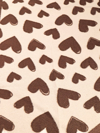 Nahaufnahme des OFF#DLY Schal Heart braun mit einem wiederholten Muster aus braunen Herzformen auf einem creme-beigen Hintergrund, Größe 180x65 cm, aus 70% Acryl und 30% Viskose gefertigt.