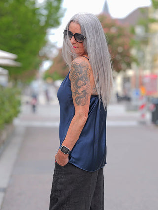 Person mit silbernem Haar trägt das OFF#DLY Top Button darkblue, ein ärmelloses, fließendes Viskose-Oberteil mit Knopfleiste, auf einem Stadtspaziergang.