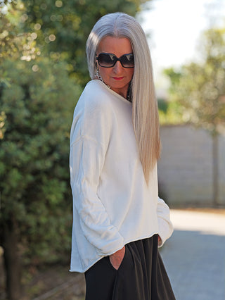 Eine Person trägt den OFF#DLY Pulli Abby white, einen locker sitzenden, weißen Baumwollpullover mit weitem Rundhalsausschnitt, der lässig über einer Schulter fällt, ideal für entspannte Looks.