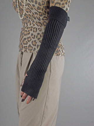 Person trägt einen schwarzen OFF#DLY Armstulpen aus Rippstrick, der vom Trizeps bis über das Handgelenk reicht, mit Daumenloch. Kombiniert mit Leoparden-Top und Perlenkette.