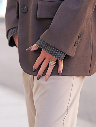 Nahaufnahme der rechten Hand mit langen, lackierten Fingernägeln, die den Lumina Blazer Schoko in Schokobraun trägt, kombiniert mit einem dunklen Karohemd und beigen Hosen.