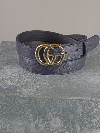 Der OFF#DLY Ledergürtel CG blue zeigt eine markante goldene Doppelkreis-G-Schnalle auf einem dunkelblauen, genarbten Leder, perfekt gefaltet auf einem grauen Block präsentiert.